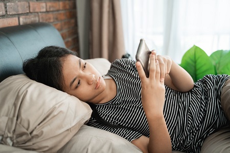 teen girl laying on bed, texting at mobile phone
