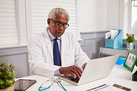 older male doctor using laptop on desk